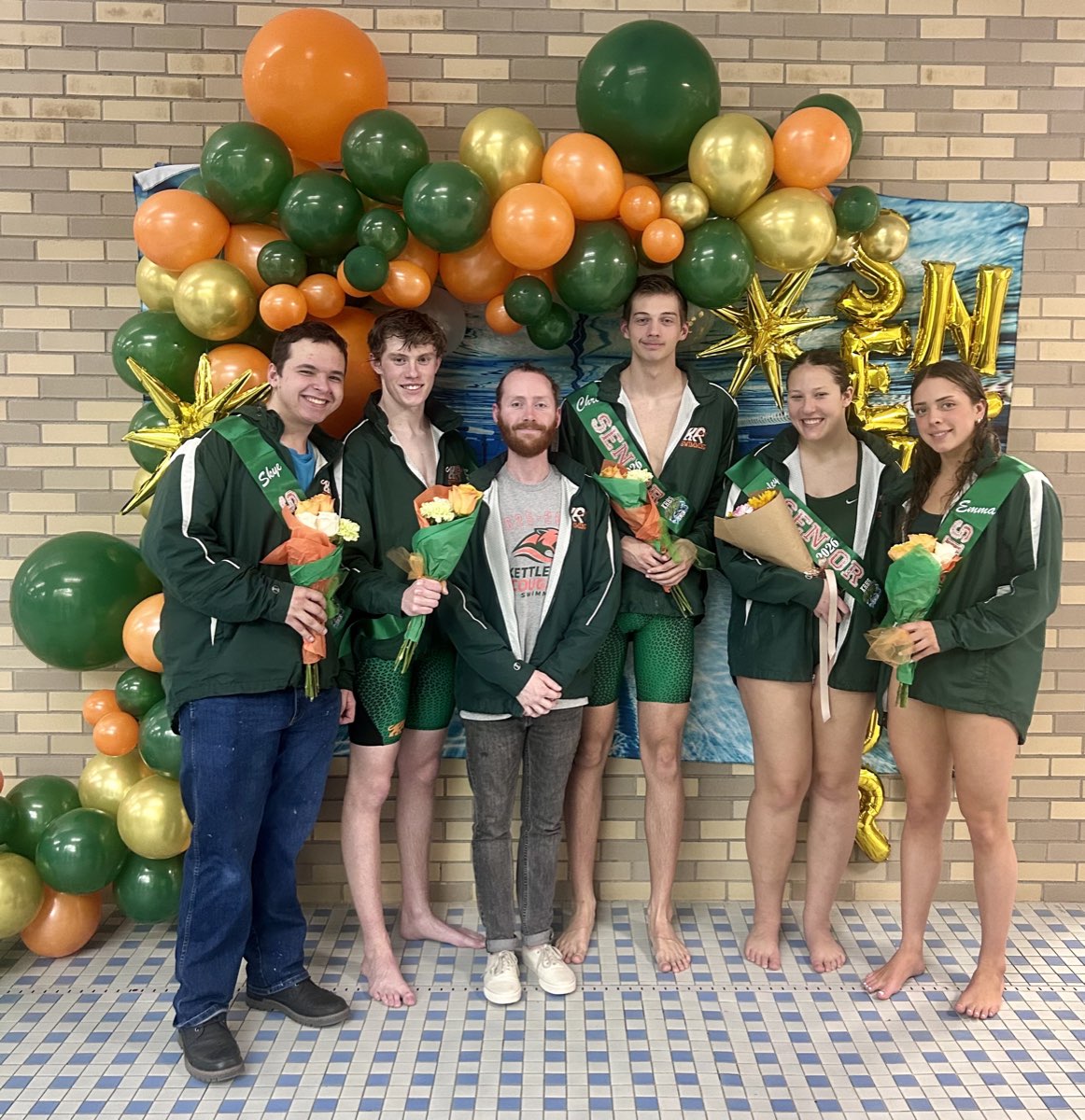 Kettle Run seniors holding flowers in front of green, orange, and gold balloons on Senior Night